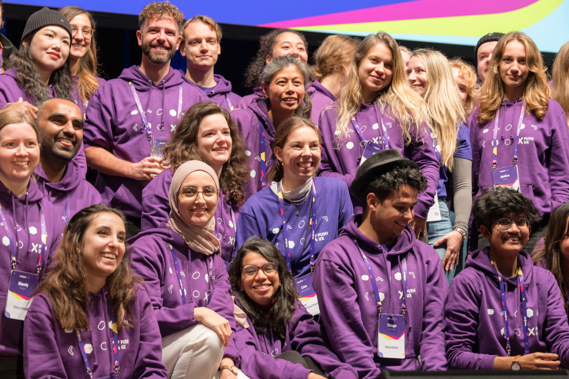 PUSH UX volunteers in purple hoodies posing together on stage at the conference.