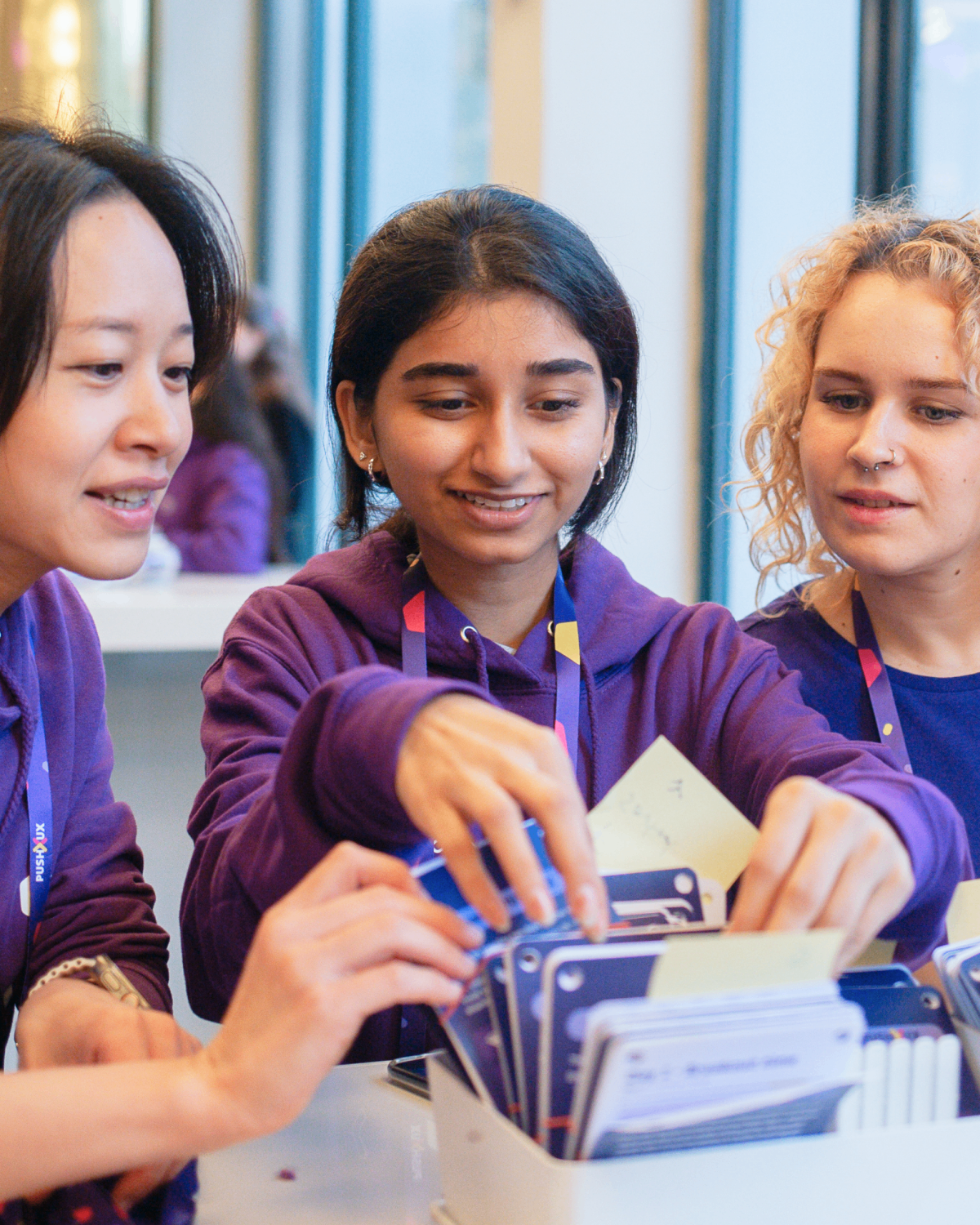 Three PUSH UX volunteers in purple hoodies smiling and organising lanyards and badges at the registration desk.