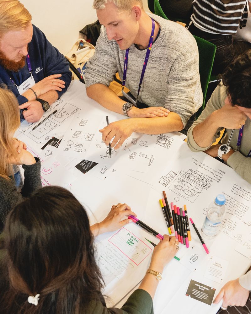 Top-down view of workshop participants sketching wireframes and ideas on large sheets of paper.