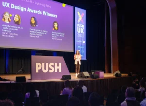 A moderator on stage in front of a slide announcing the upcoming lightning talk speakers.