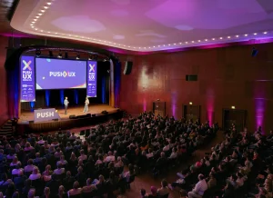 Wide shot of the main stage, showing a large audience watching a speaker and moderator.